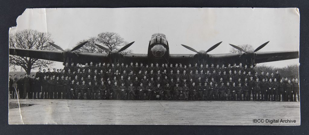 Four rows of personnel standing and sitting in front of a Lancaster. In the background, trees. 